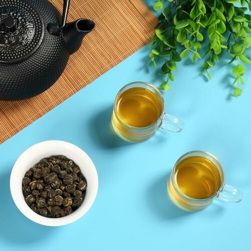 Tea set with teapot, cups, and loose tea leaves on a blue background.